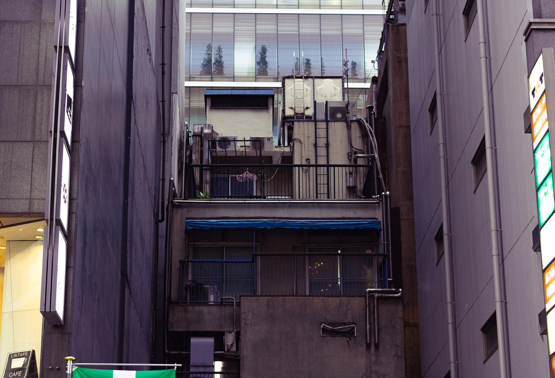 Grungy concrete building squeezed between two other buildings on the side of the frame with their shadows casted on it.